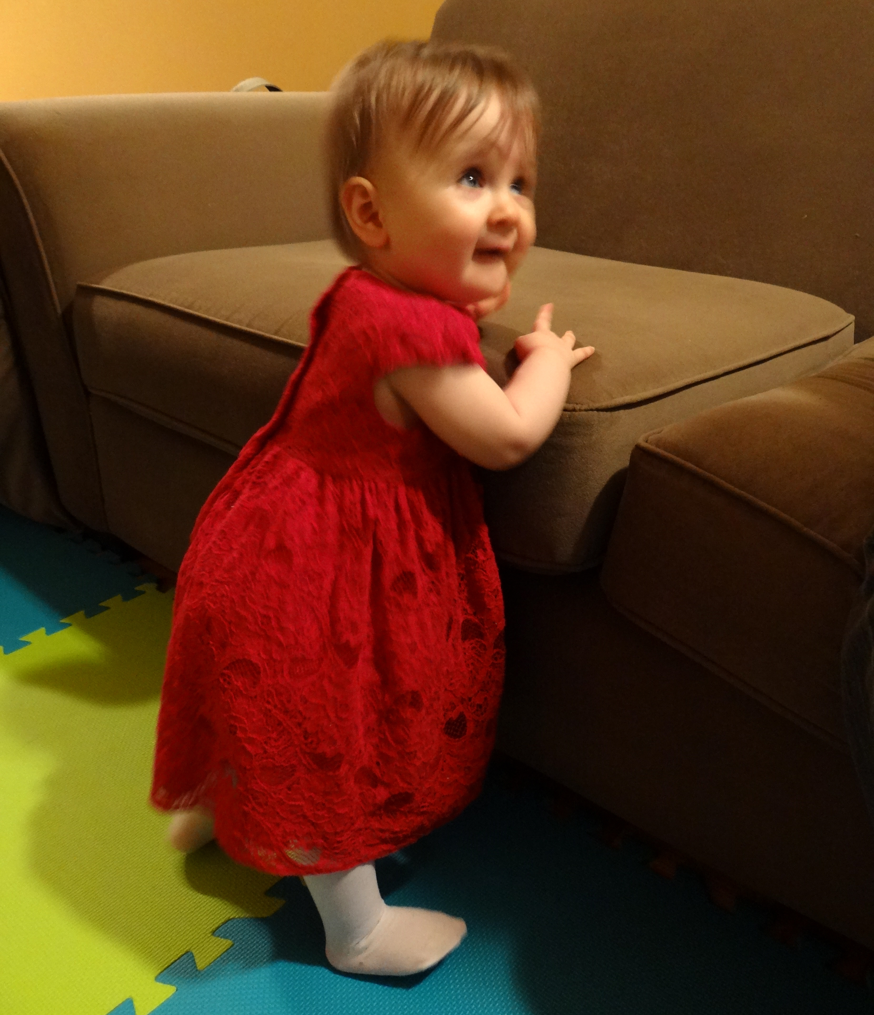Baby girl in a red dress standing on her own